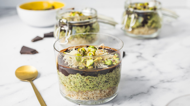 Close up on a cup of Dubai style pistachio chia pudding with spoon and more in background.