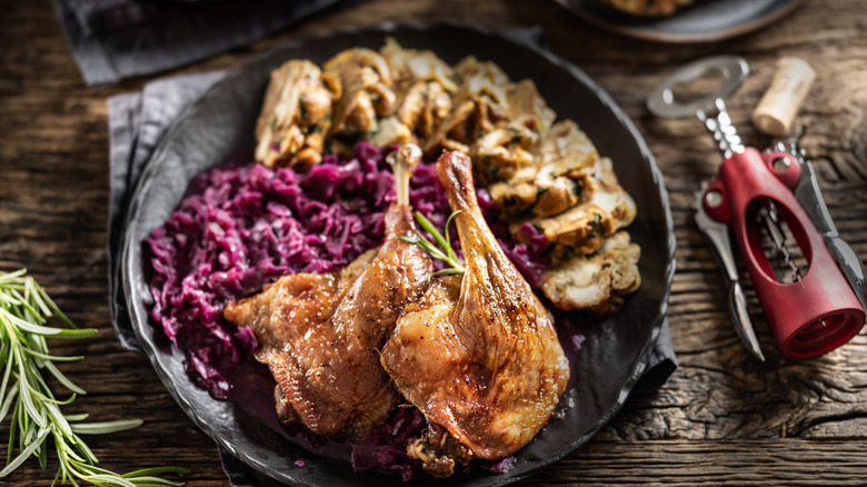 two roasted duck legs on a plate with vegetables