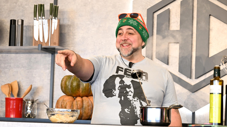Duff Goldman in a mock kitchen pointing at something behind the camera