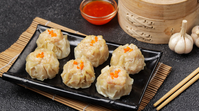 A plate full of dumplings with chili sauce and garlic pods