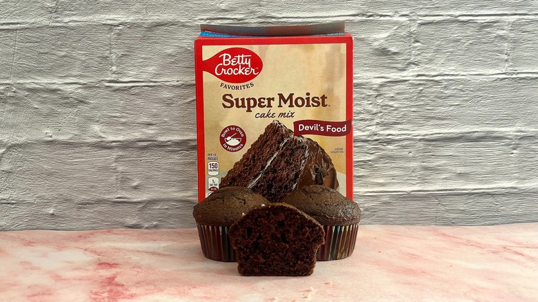 Box of Betty Crocker Devil's Food cake mix behind three cupcakes on grey background