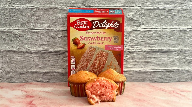 Box of Betty Crocker strawberry cake mix behind three cupcakes on grey background