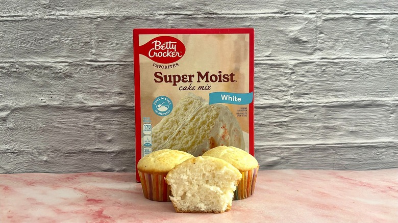 Box of Betty Crocker White cake mix behind three cupcakes on grey background