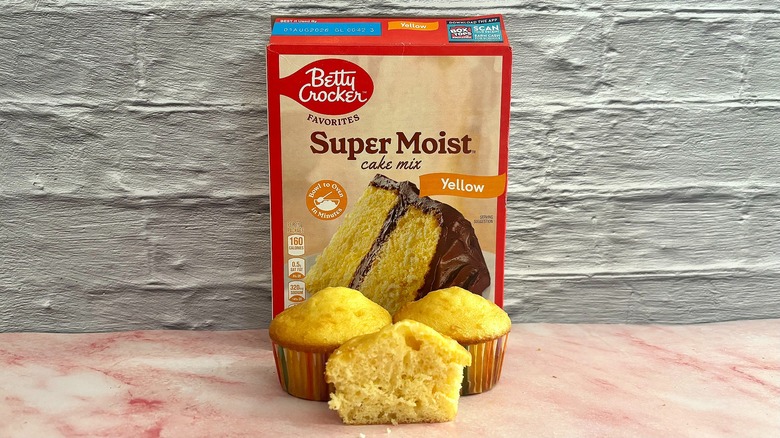 Box of Betty Crocker Yellow cake mix behind three cupcakes on grey background