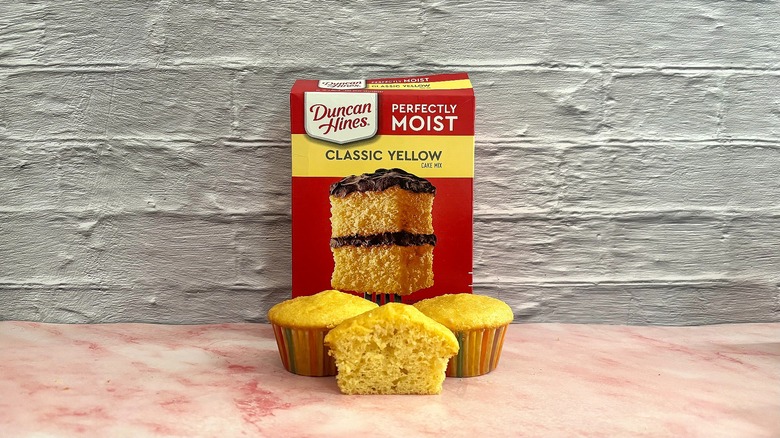 Box of Duncan Hines Classic Yellow cake mix behind three cupcakes on grey background
