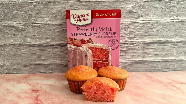 Box of Duncan Hines Strawberry Supreme cake mix behind three cupcakes on grey background