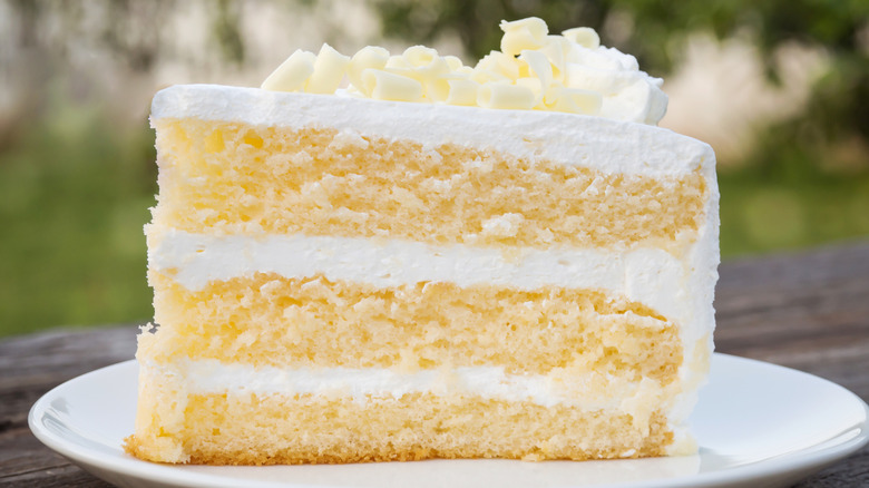 A close up of a slice of vanilla cake with white buttercream frosting and white chocolate curls