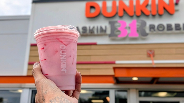 A hand holding the Parke Daydream Refresher in front of the Dunkin' storefront
