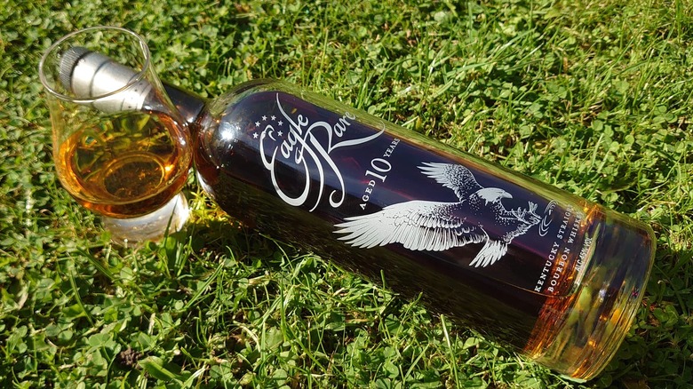 A bottle of Eagle Rare 10-year laid down on grass besides a full glass