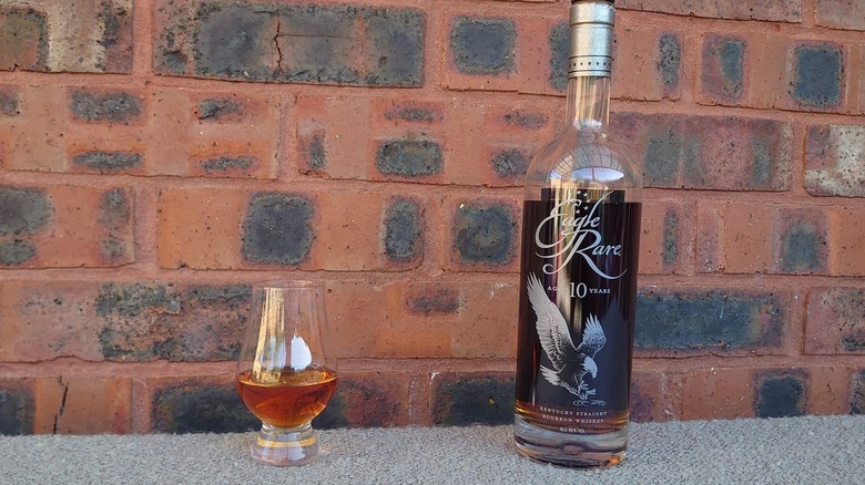 A bottle and glass of Eagle Rare 10-year in front of a plain brick background