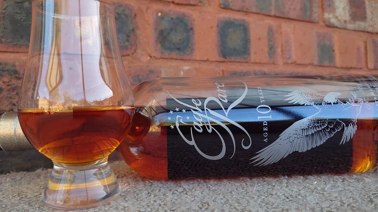 A close up of a glass of Eagle Rare 10-year with the bottle laying on its side in the background