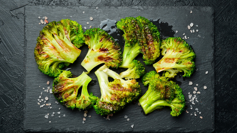 Florets of roasted broccoli on dark gray surface with crystals of sea salt