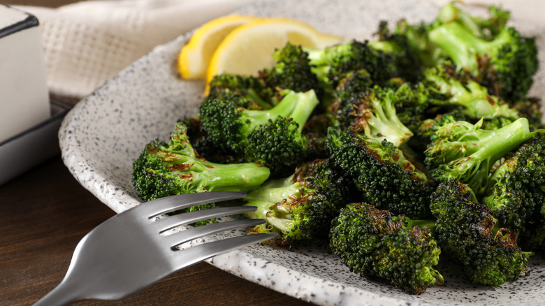 Roasted broccoli on square speckled plate with silver fork and lemon slices