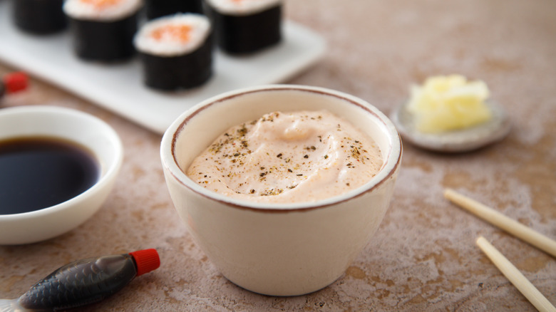 Mayonnaise dip with pepper in white bowl next to sushi rolls, dish of soy sauce, and grated ginger