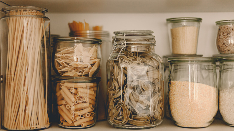 Row of glass jars holding pasta and dry flour on shelf