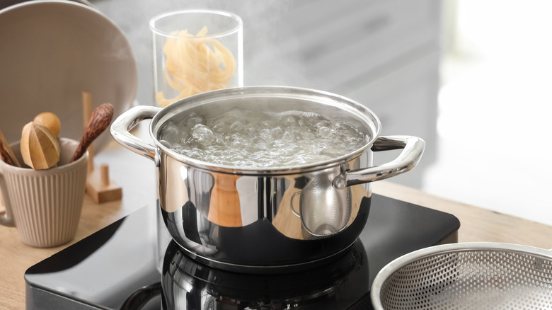 A woman goes to grab a pot that's boiling over on a stove