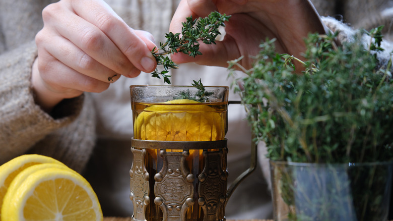 Hands stripping thyme over a glass of tea with lemon