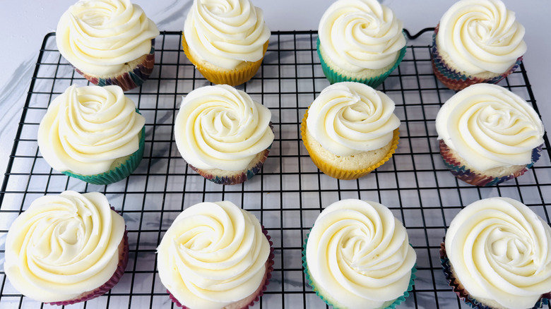 white-frosted cupcakes in paper liners sitting on a wire rack