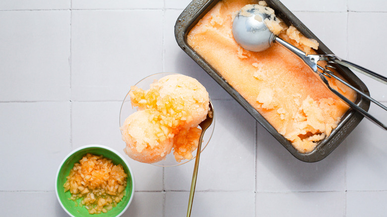 A glass of cantaloupe sorbet sits beside a container of ice cream in the back