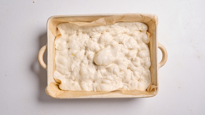 dimpling the dough with fingers in a baking dish