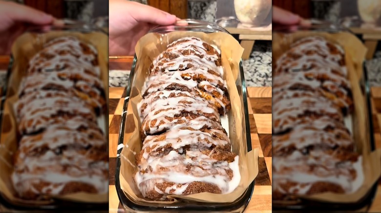 A close-up of a woman holding a glass baking dish containing a pull-apart pumpkin cinnamon bread with a sugar glaze