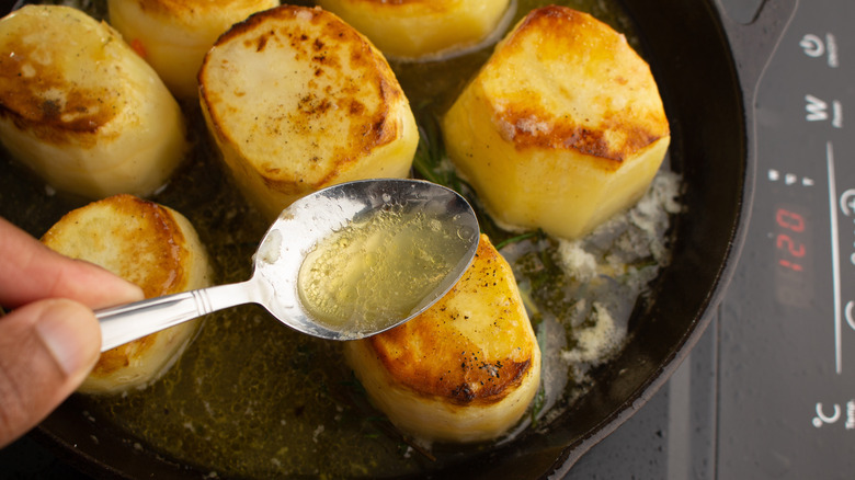 spooning broth over potatoes