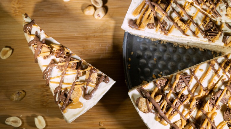 Peanut butter ice cream pie with single slice taken out on wood surface surrounded by peanuts