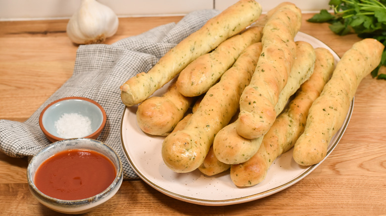 garlic and herb breadsticks piled on plate with dipping sauce