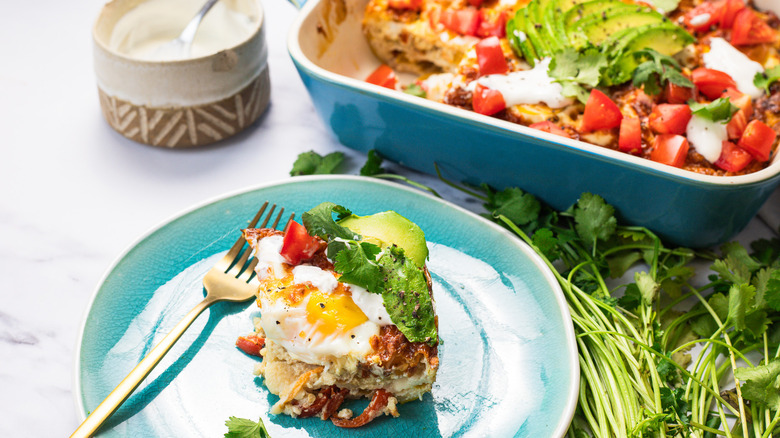 A serving of easy tortilla breakfast casserole on a blue plate with casserole in background.
