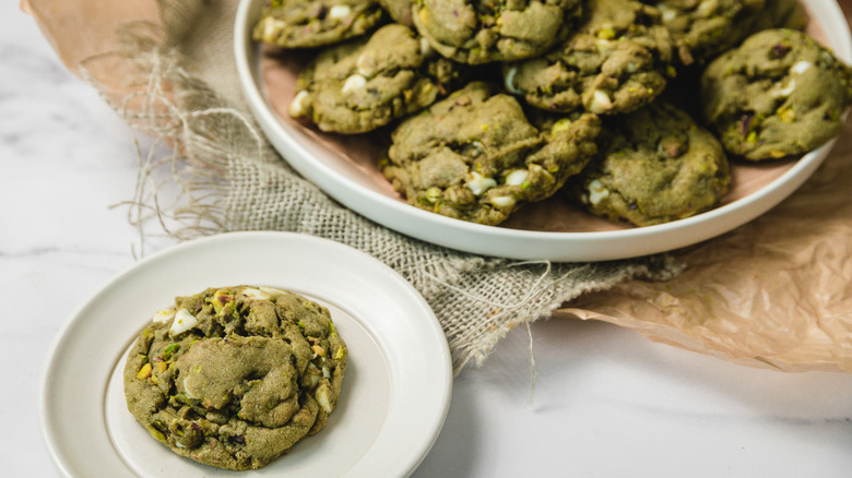 White chocolate matcha cookie on white plate before a platter with cookies
