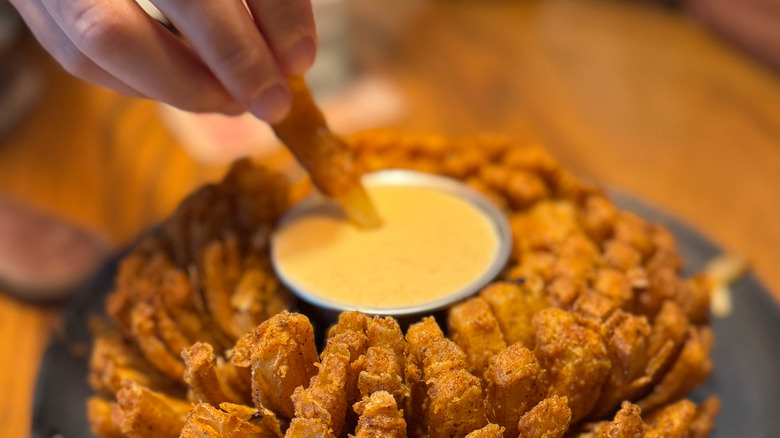 A hand dips a piece of Bloomin' Onion into a container of dip