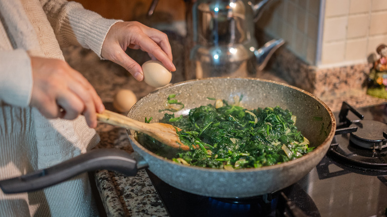 A person making a spinach omelet in a pan on the stove