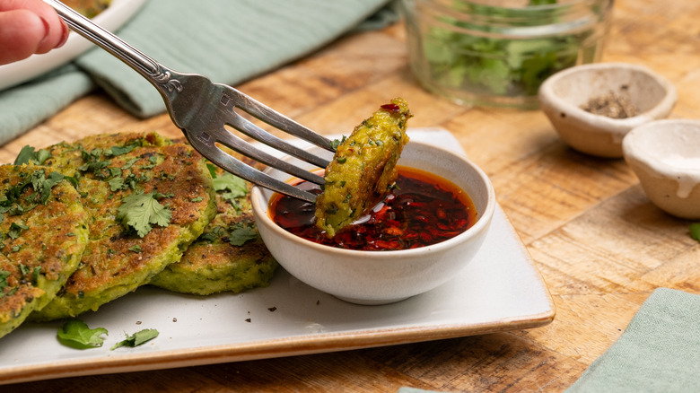 Fork dunking edamame fritter into soy dipping sauce