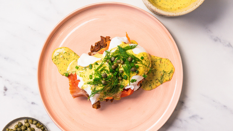 Overhead view of eggs Norwegian with rosti and dill hollandaise on a pink plate.