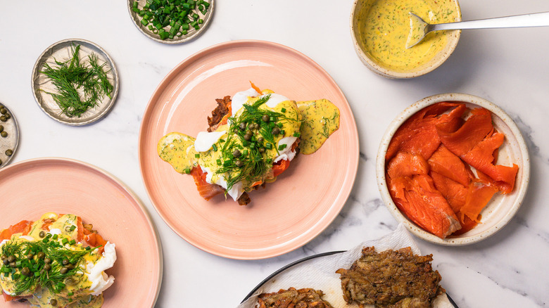 Two plates of eggs Norwegian with rosti and dill hollandaise, surrounded by toppings.