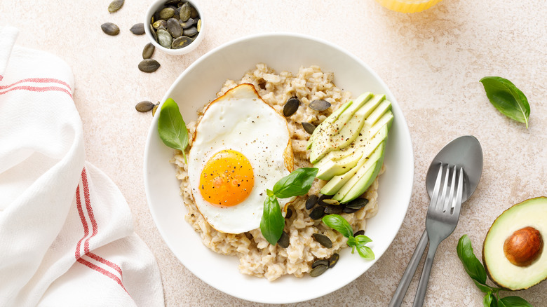 A healthy breakfast bowl with oatmeal, fried egg, and sliced avocado