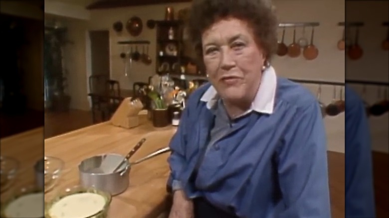 Julia Child sitting in front of a kitchen counter with a pot on it