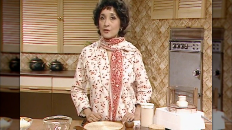 Madhur Jaffrey in front of a counter with a food processor and bowls