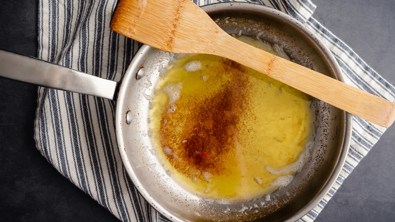 Stainless steel skillet of browned butter with a wooden spatula resting on the rim