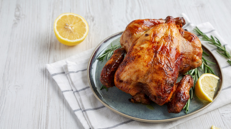 Rotisserie chicken on a plate with rosemary and lemon