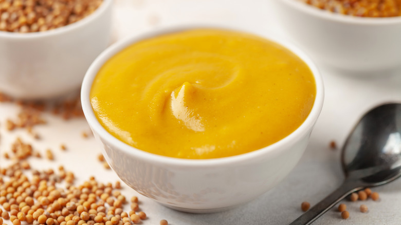 Bowl of mustard surrounded by mustard seeds