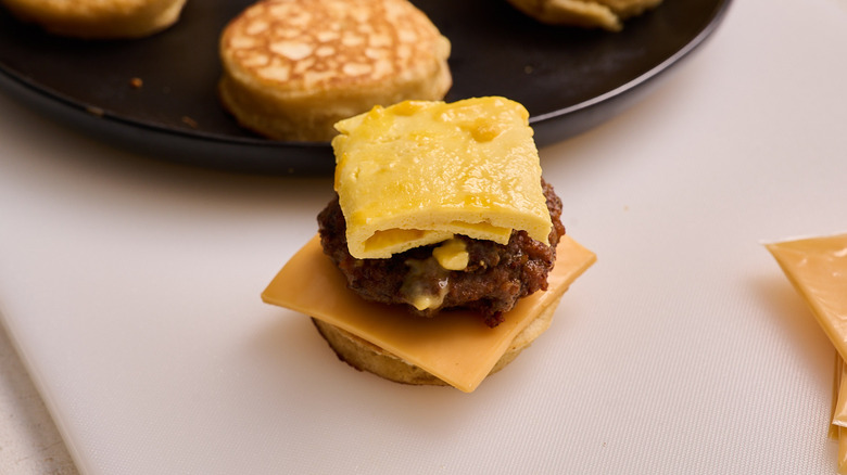 stacking griddle cakes, sausage, and egg on a cutting board