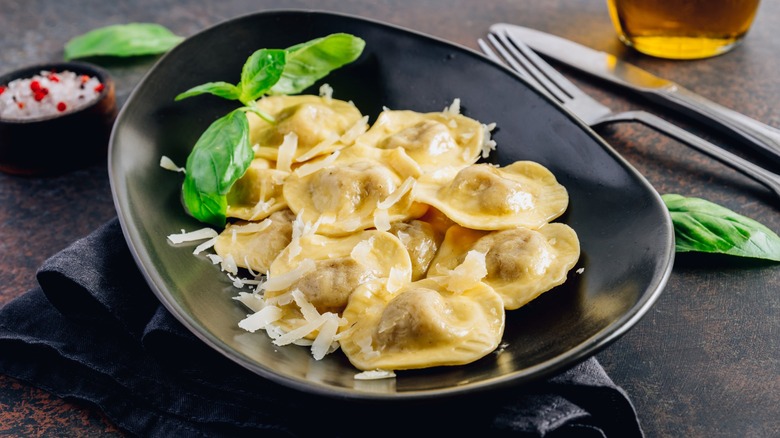 ravioli with parmesan and basil leaves on a black plate