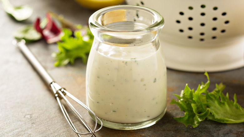Glass bottle of ranch dressing next to whisk and lettuce