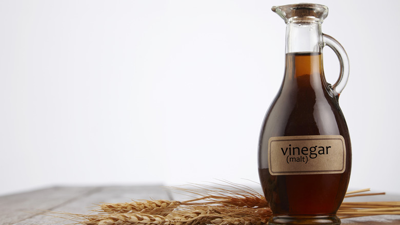 Malt vinegar in a labeled bottle on a table with barley grain