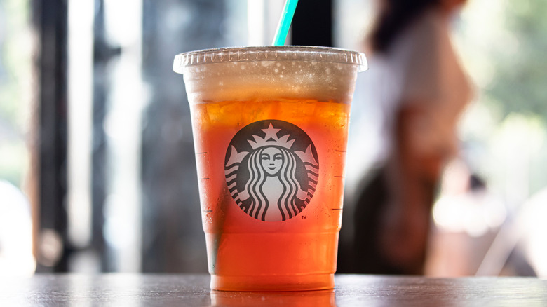Hand holding a Starbucks Paradise Refresher topped with cold foam by orange flowers