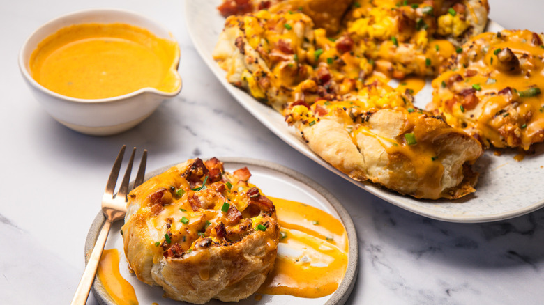 Close up on an eggs Benedict roll on a plate with hollandaise sauce and more rolls in background