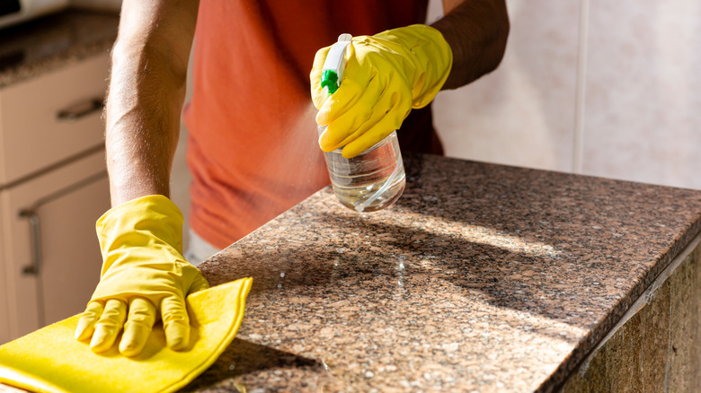 person wipes a granite surface with a cloth and bottle
