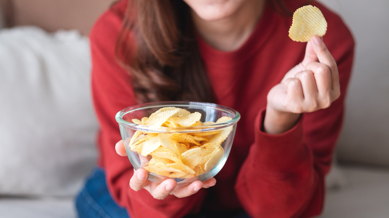 Woman holding bowl of chips and one chip in hand