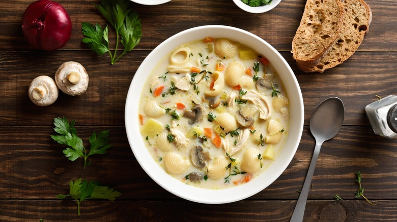 a bowl of chicken noodle soup with mushrooms on a wood background